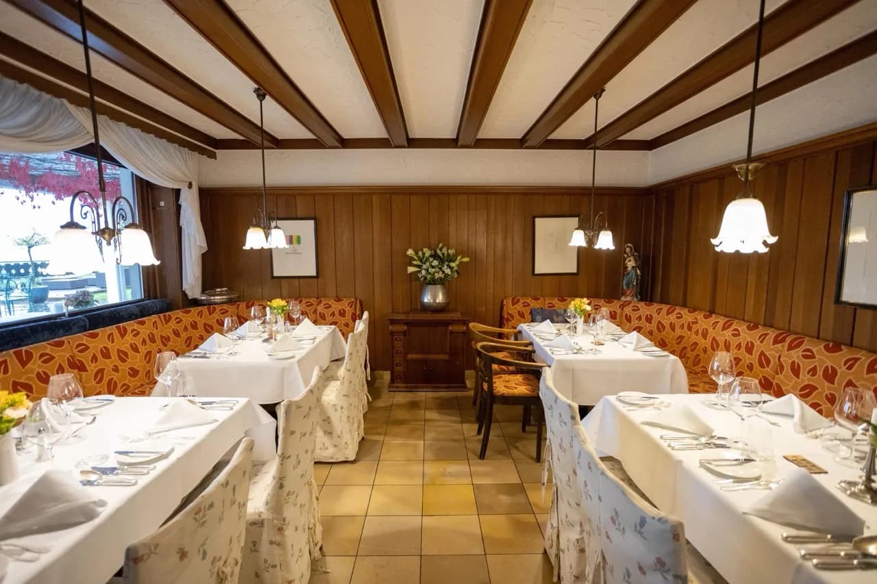 Gemütliches Restaurant mit Holzwänden, weißen Tischdecken, floral bezogenen Stühlen und herabhängenden Lampen.